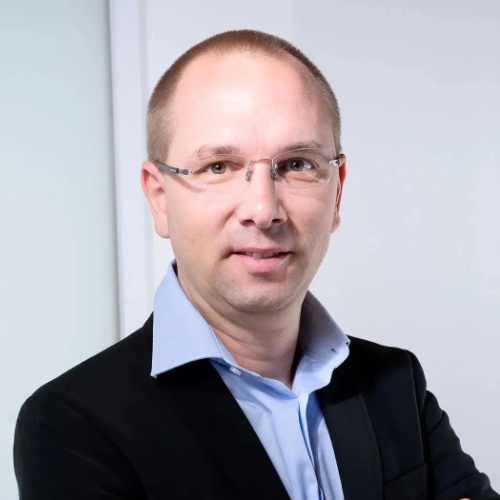 Das Bild zeigt einen Mann mit Brille, der ein blaues Hemd und ein schwarzes Sakko trägt