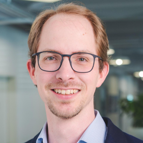 Ein Mann mit Brille und Anzug lächelt freundlich in die Kamera.