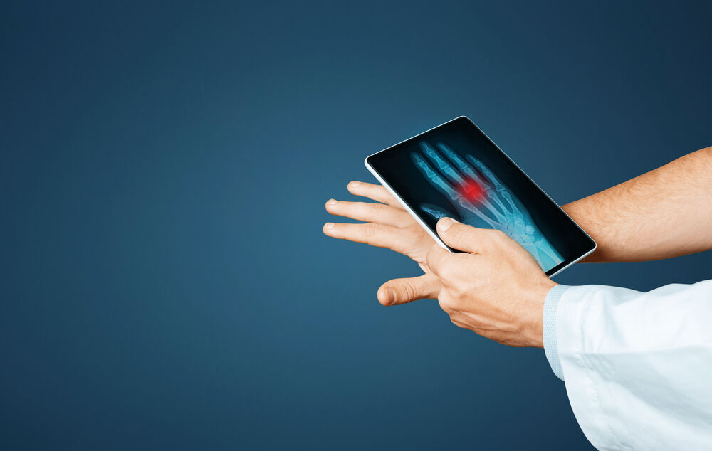 Hand mit ausgestreckten Fingern, darüber ein Tablet mit Röntgenbild der Hand und rotem Markierungsbereich