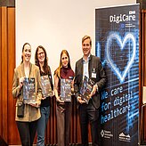 Bild zeigt vier Personen, die nebeneinander stehen und jeweils eine Auszeichnung oder Plakette in den Händen halten.