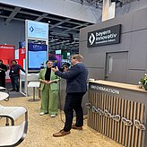 Auf dem Bild ist ein Mann und eine Frau zu sehen, welche eine Ansprache halten und vor einer Theke stehen.