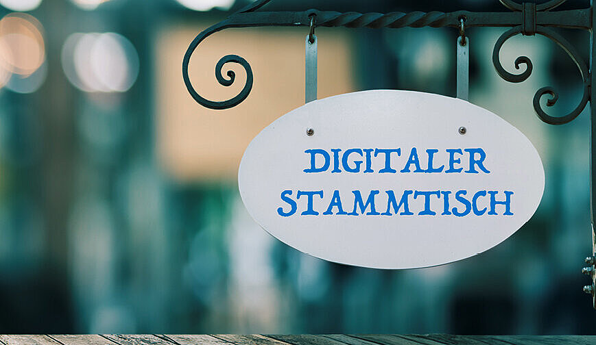 Auf dem Bild ist ein Schild "Digitaler Stammtisch" zu sehen, der Hintergrund ist verschwommen