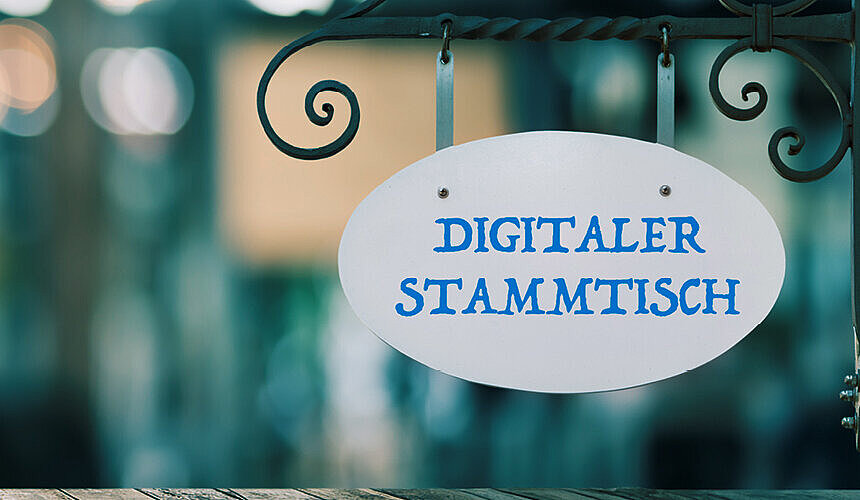 Auf dem Bild ist ein Schild "Digitaler Stammtisch" zu sehen, der Hintergrund ist verschwommen