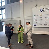 Auf dem Bild sind drei Personen zu sehen, welche sich vor einer Pressewand in einer Veranstaltungslocation unterhalten.