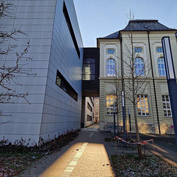 Zwei angrenzende Gebäude, links ein moderner Bau, rechts ein historischer. 