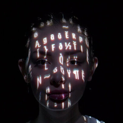 Frau die mit einem Beamer mit Buchstaben angestrahlt wird