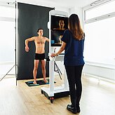 Fachkraft arbeitet an einem medizinischen Gerät, während eine stehende Person davor positioniert ist.