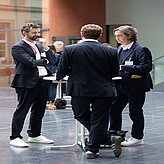 Mehrere Männer stehen um einen Tisch und diskutieren.