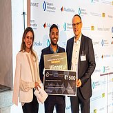 Drei Personen halten gemeinsam ein großes Scheckbrett mit der Aufschrift '10.000 Euro' und der Empfängerangabe 