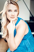 Eine junge Frau mit langen, blonden Haaren blickt direkt in die Kamera. Sie trägt ein blaues schulterfreies Kleid.