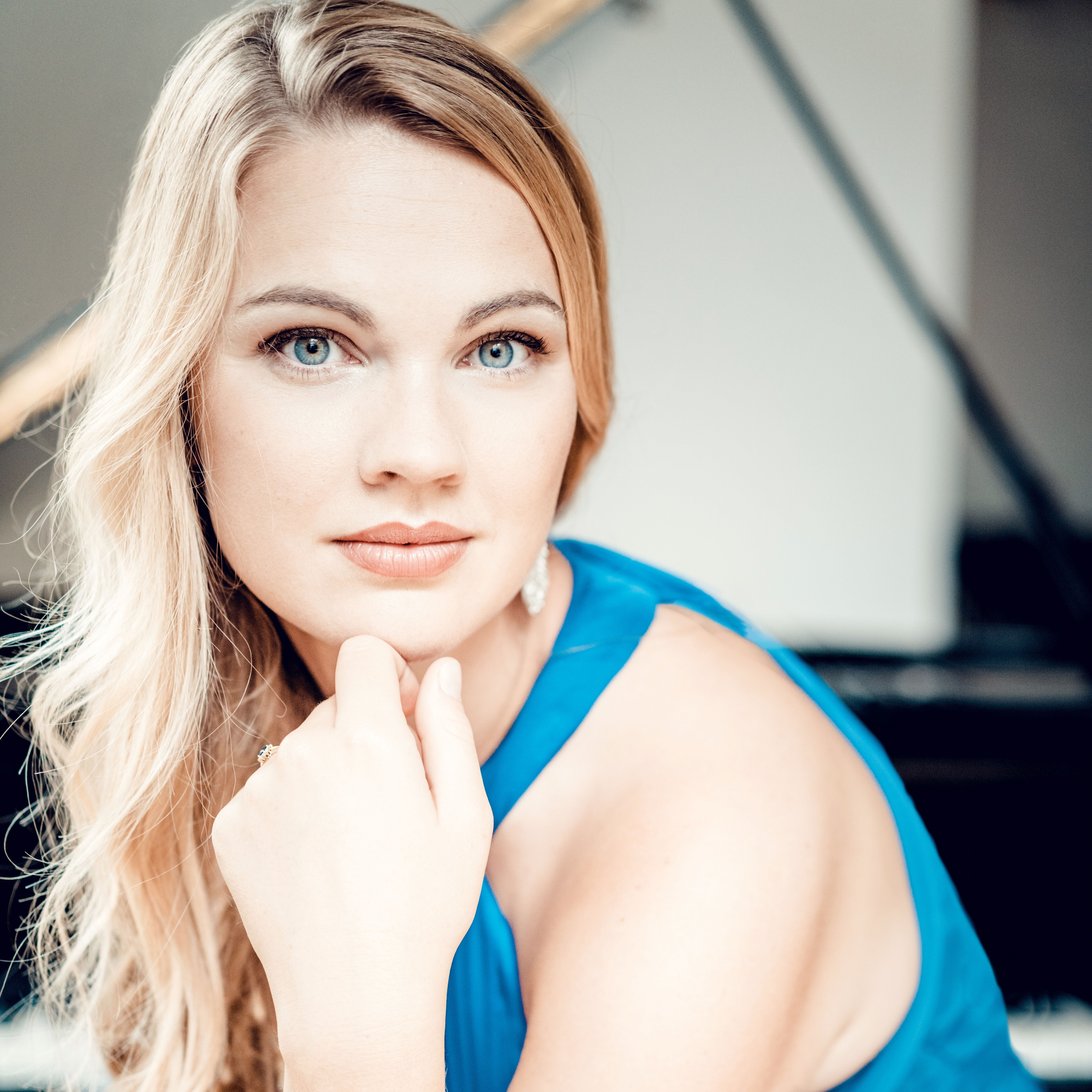 Eine junge Frau mit langen, blonden Haaren blickt direkt in die Kamera. Sie trägt ein blaues schulterfreies Kleid.