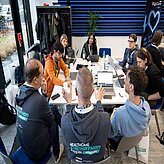 Mehrere Personen arbeiten an Laptops, während sie an einem Tisch zusammensitzen und Ideen austauschen.