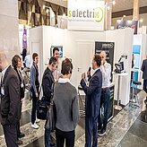 Das Bild zeigt eine Gruppe von Personen an einem Messestand oder Ausstellungsbereich mit dem Schriftzug „solectrix“ am oberen Rand. Mehrere Personen unterhalten sich oder betrachten die ausgestellten Produkte und Informationen im Standbereich. 