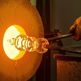 Glasbläser formt ein glühendes Werkstück an einer Ofenöffnung während des künstlerischen Glasbearbeitungsprozesses.