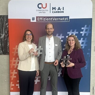 Drei Teilnehmende vor einem Banner mit Hashtag Figuren in der Hand