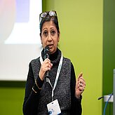 Eine Frau hält einen Vortrag, sie steht vor einem grünen Hintergrund