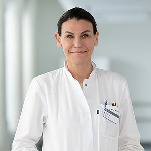 Person in weißem Arztkittel mit Namensschild und Stiften in der Brusttasche vor unscharfem Hintergrund