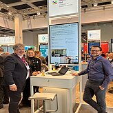 Auf dem Bild sind zwei Herren zu sehen, welche vor Ihrem Messestand posieren.