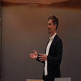 Redner gestikuliert während eines Vortrags beim Bayerischen Batteriekongress 2025.