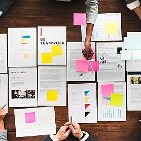 Sechs Personen beraten sich an einem Tisch auf dem Papiere ausgebreitet sind