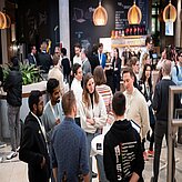 Menschen stehen um Stehtische und unterhalten sich 