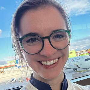 Frau mit Brille vor Flughafen im Hintergrund