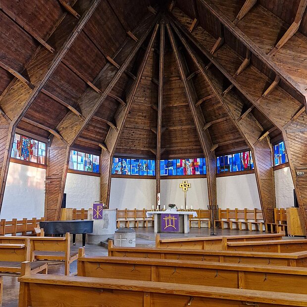 Kirchenraum von innen mit Holzkuppel, bunten Glasfenstern und Blick auf den Altar.