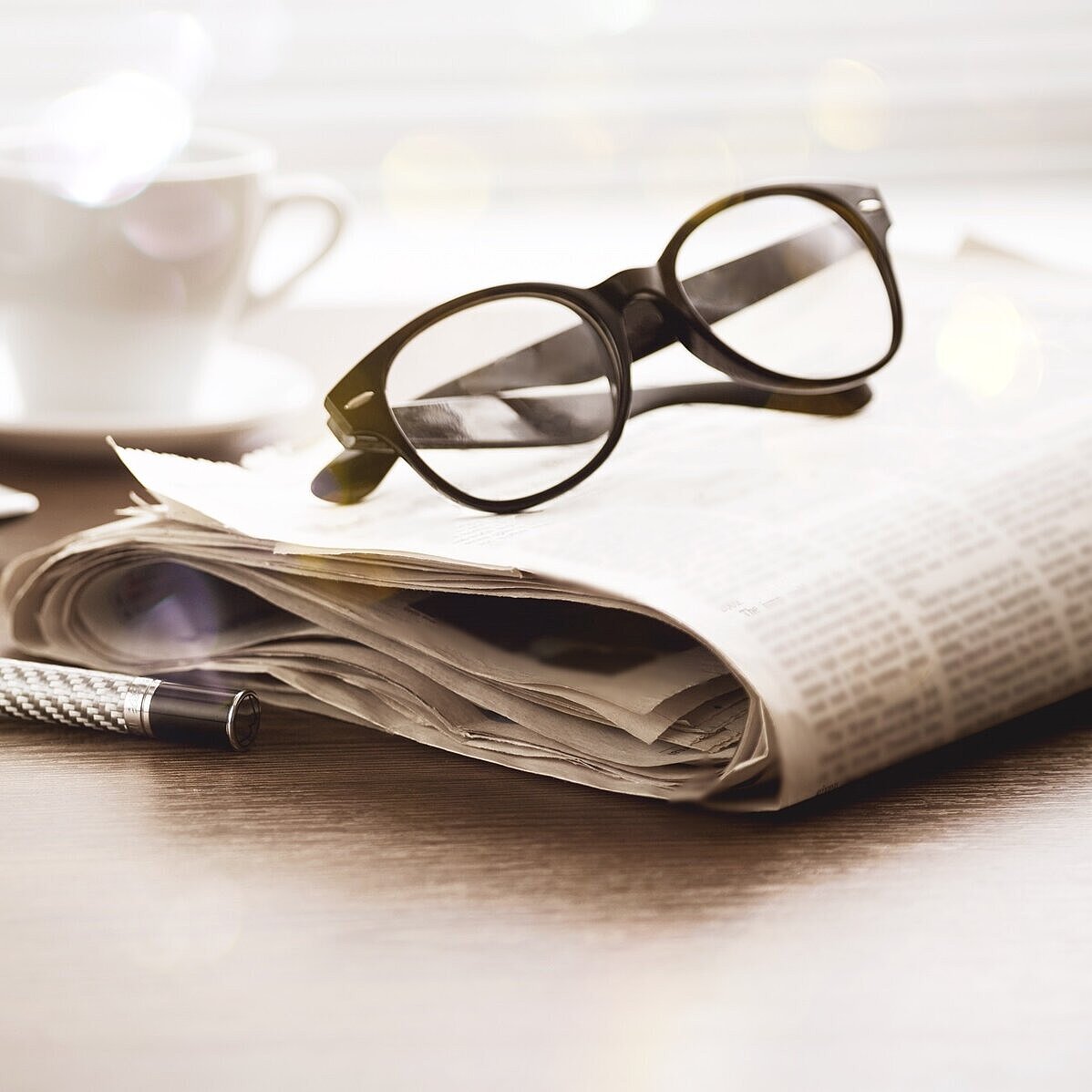 Auf einer zusammengerollten Zeitung liegt eine Brille und daneben liegt ein Stift
