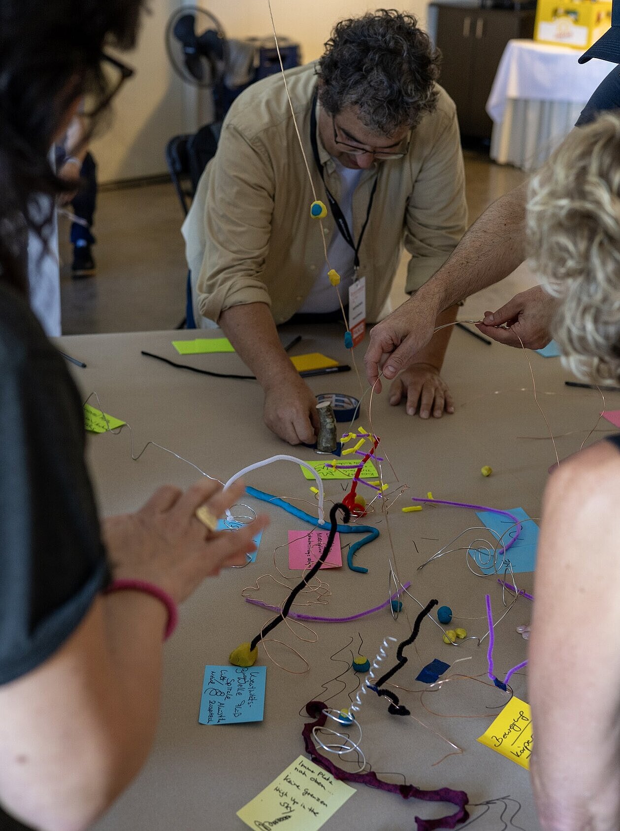 Mehrere Personen arbeiten gemeinsam an einem Tisch. Auf der Tischoberfläche liegen neben Notizzetteln auch Bastelutensilien wie Knete, mit denen die Teilnehmenden verschiedene Formen gestalten.