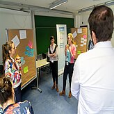 Mehrere Personen stehen in einem Raum vor zwei Pinnwänden mit bunten Zetteln und diskutieren.