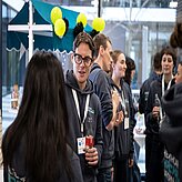 Das Bild zeigt eine Gruppe von Menschen, die wahrscheinlich an einem Event oder einer Konferenz teilnehmen. Die meisten tragen passende Kapuzenpullover mit einem Logo und Namensschilder.