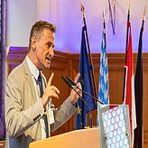 Ein Mann hält eine Rede am Rednerpult und spricht zu einem Publikum