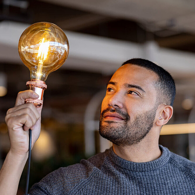 Mann hält eine leuchtende Glühbirne in der Hand hoch