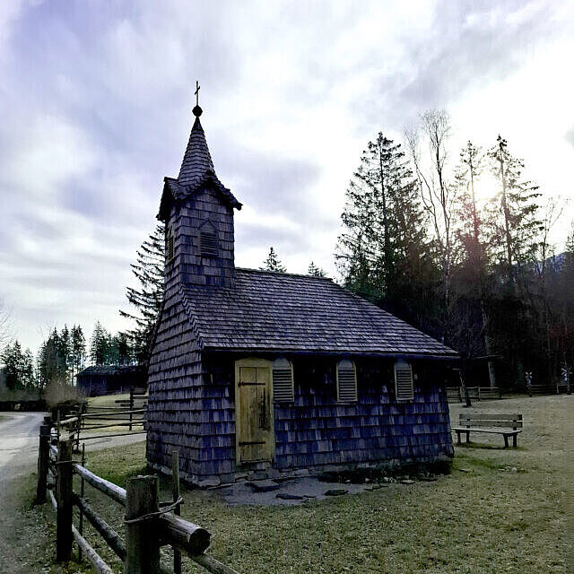 Holzkirche auf einer grünen Wiese, umrandet von einem Holzzaun. 