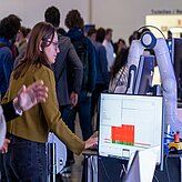 A booth on the Thinknet 6G Summit, with a woman puting data into a PC to steer a robotic arm.