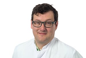 Person in weißem Hemd steht vor einem hellen Hintergrund in einem modernen Innenraum.