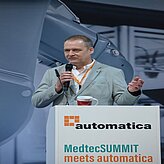 Eine Person steht hinter einem Rednerpult und spricht in ein Mikrofon. Auf dem Pult stehen Schriftzüge