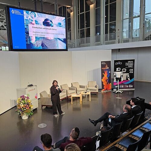 Ausblick CreativeTech 2026: Johanna Lison, Projektmanagerin des CreativeTechHUB, Bayern Innovativ GmbH, spricht vor Publikum in ein Mikrofon.