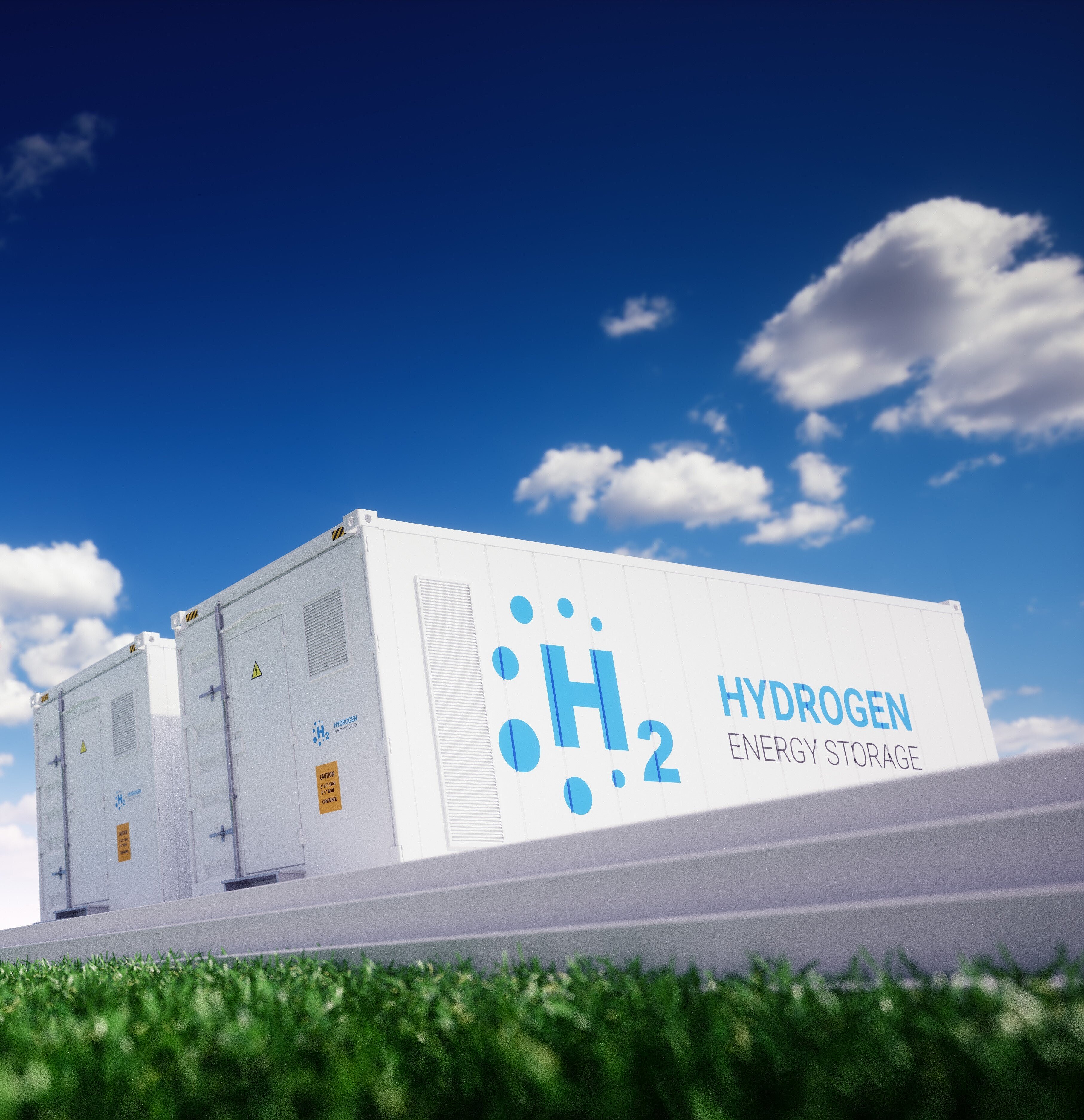 Das Bild zeigt weiße Container mit der Aufschrift „H₂ Hydrogen Energy Storage“ auf einer Anlage im Freien.