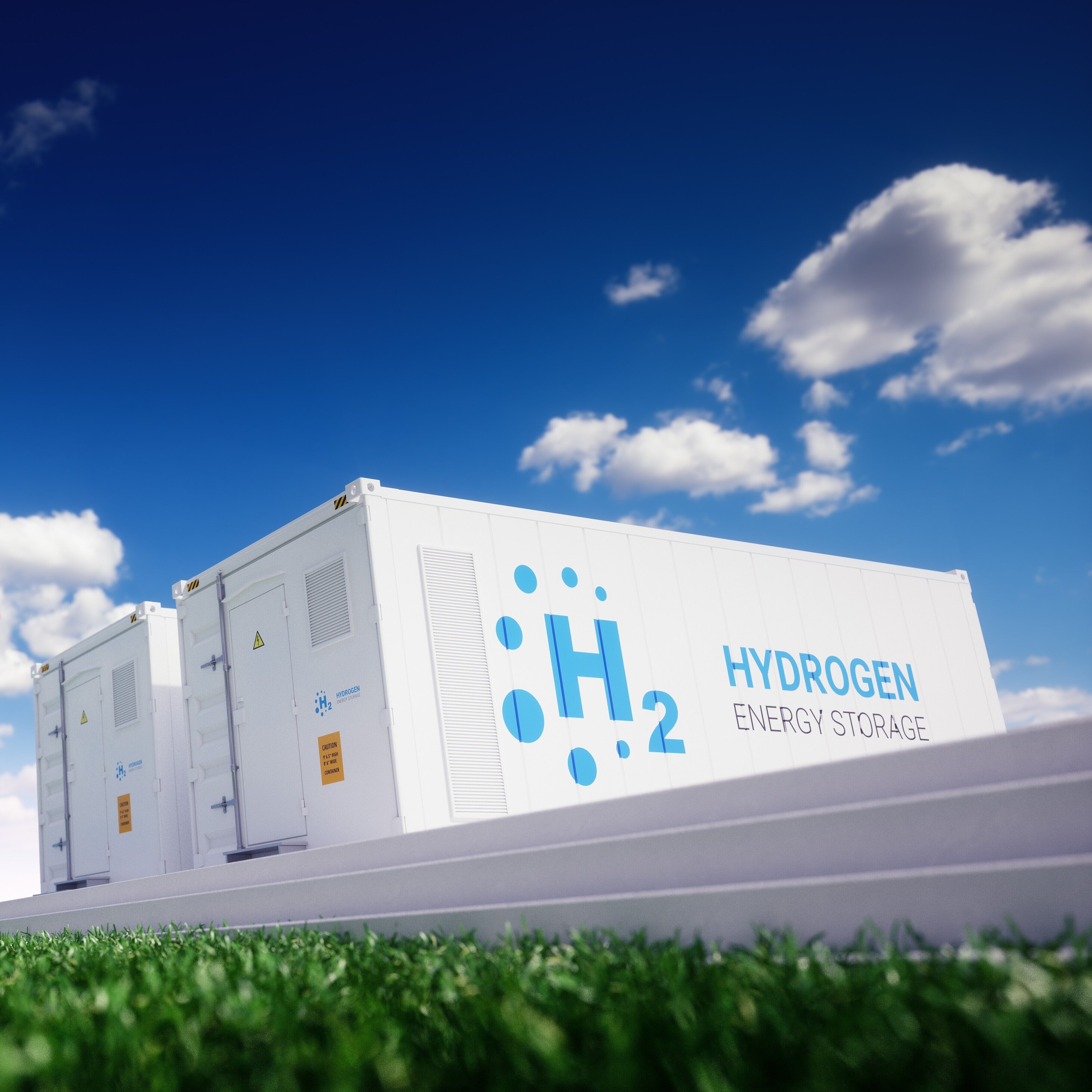 Das Bild zeigt weiße Container mit der Aufschrift „H₂ Hydrogen Energy Storage“ auf einer Anlage im Freien.