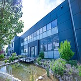 Modernes Firmengebäude mit großer Glasfassade, davor ein Teich und umgebende Bepflanzung