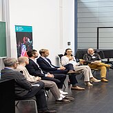  Eine Gruppe von Menschen sitzt auf einer Bühne und diskutiert miteinander.