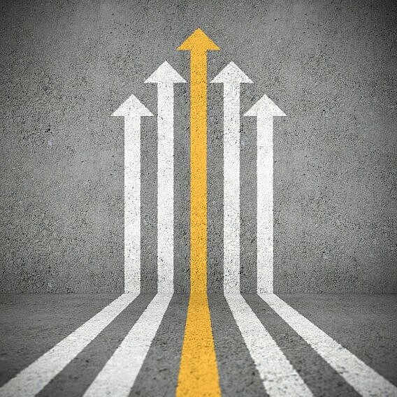 Fünf aufgemalte Pfeile auf Asphalt, wobei ein zentraler gelber Pfeil symbolisch herausragt und nach oben führt.
