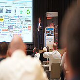 Präsentation über Bayerns Batterie-Ökosystem mit zahlreichen Unternehmenslogos beim Bayerischen Batteriekongress 2025.