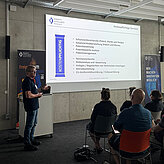 Bruno Götz, Leiter Patente und Normen bei der Bayern Innovativ GmbH, steht neben dem Rednerpult und referiert vor den Teilnehmenden des Meet-ups und zeigt die wichtigsten Schutzrechte für Kultur- und Kreativschaffende auf. Im Hintergrund sind ein Roll-up und eine Leinwand zu sehen.