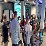 Auf diesem Bild ist eine Gruppe von Menschen zu sehen, die in einem Halbkreis stehen und sich unterhalten oder diskutieren.