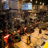 Gruppe von Personen mit Schutzhelmen steht in einer Industriehalle mit glühenden Maschinen und Produktionsanlagen im Hintergrund. Das Foto entstand während der Delegationsreise in Kanada.