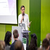 Ein Mann hält einen Vortrag vor einem grünen Hintergrund