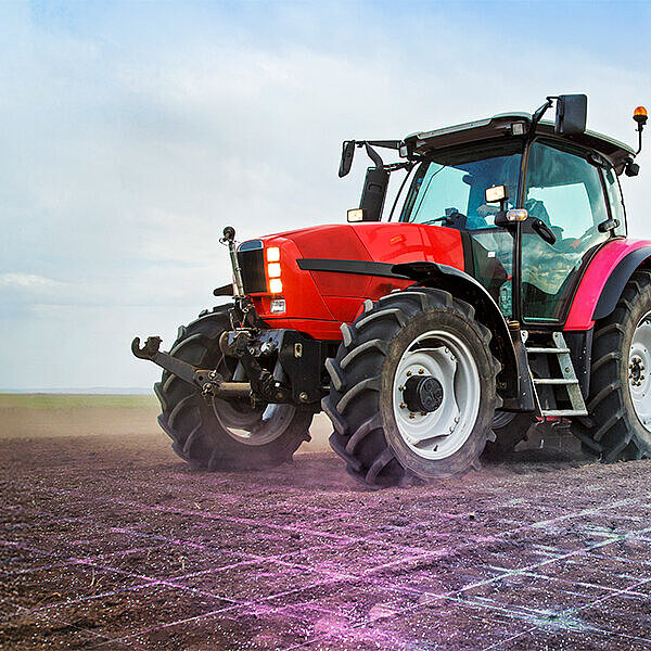Ein Traktor steht auf einem Feld, das mit einem Datengitter versehen ist. Daneben fliegt eine Drohne.