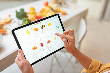 Zwei Hände halten ein Tablet auf dem der Onlineshop eines Obst- und Gemüse-Händlers zu sehen ist